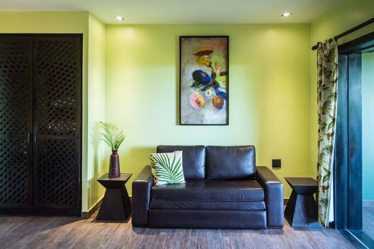 Una sala de estar moderna con un sofá de cuero negro, un cuadro abstracto enmarcado y una planta en maceta.