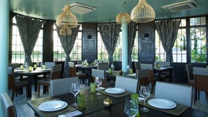 Restaurante con varias mesas dispuestas para comer, con cortinas a estampado de cebra y lámparas colgantes de madera.