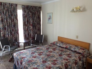 Une chambre d’hôtel avec un lit, deux chaises, une petite table et un tableau au mur.