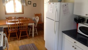 A compact kitchen with a dining table, chairs, a refrigerator, a microwave, and a small potted plant.