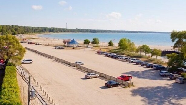 A beachside parking lot with cars, a sandy area, and a view of the sea.