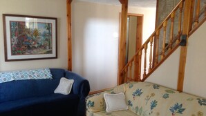 A living room with two sofas, one dark blue and one floral-patterned, a wooden staircase, and a framed picture on the wall.