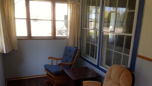 A room with a wooden floor, a blue upholstered chair, a wooden table, and a beige armchair.