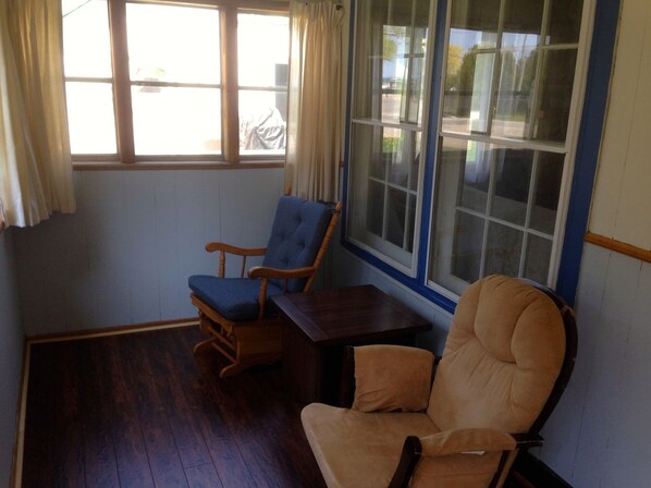 A room with a wooden floor, a blue upholstered chair, a wooden table, and a beige armchair.