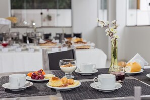 A breakfast setting with a variety of food items on plates, including fruits, pastries, and a glass of juice. - Domum Hotel (Pindamonhangaba)