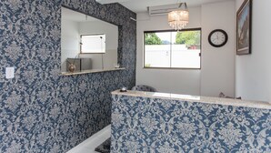 Un bagno con carta da parati decorata, uno specchio, un orologio e una finestra con vista.