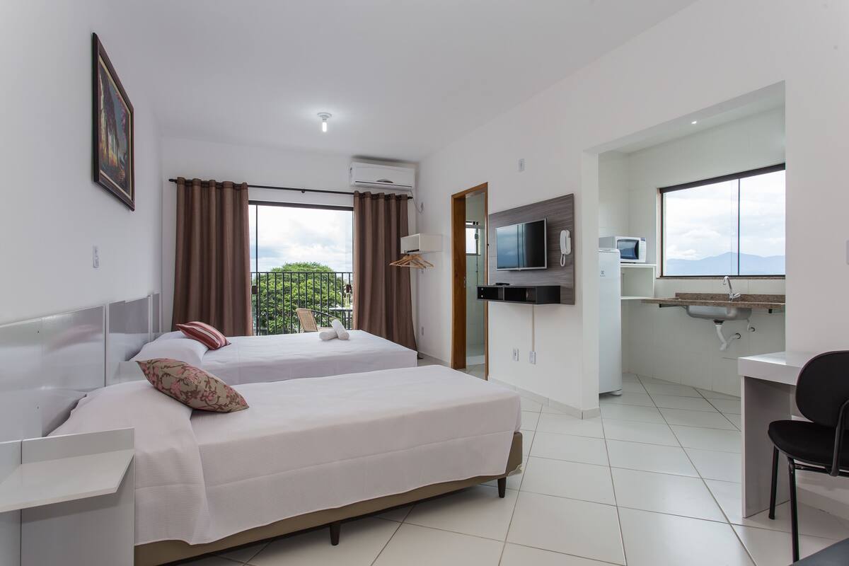 A hotel room with two beds, a desk, a TV, and a view of the outdoors.