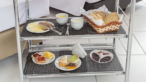 Un carrello per la colazione con diversi cibi e bevande in una camera d'hotel.