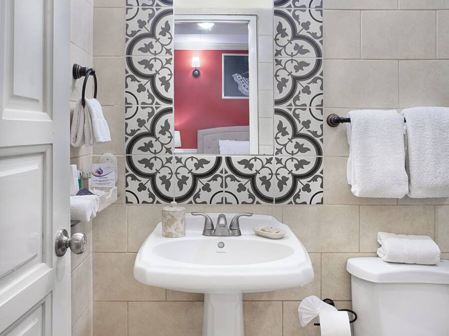 A bathroom with a pedestal sink, a toilet, a trash bin, and a mirror with decorative tiles.