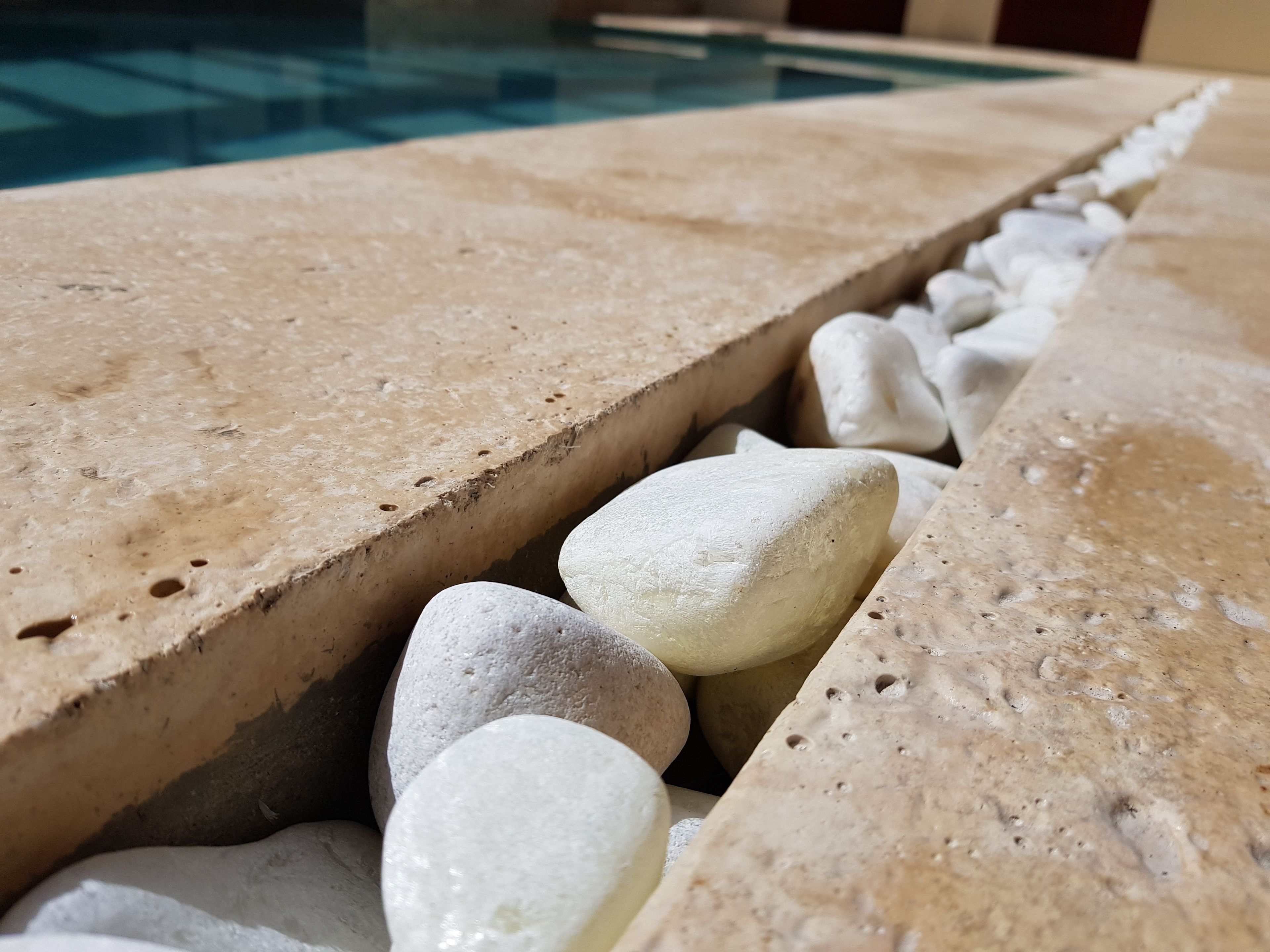 A poolside area with a stone edge and smooth pebbles.