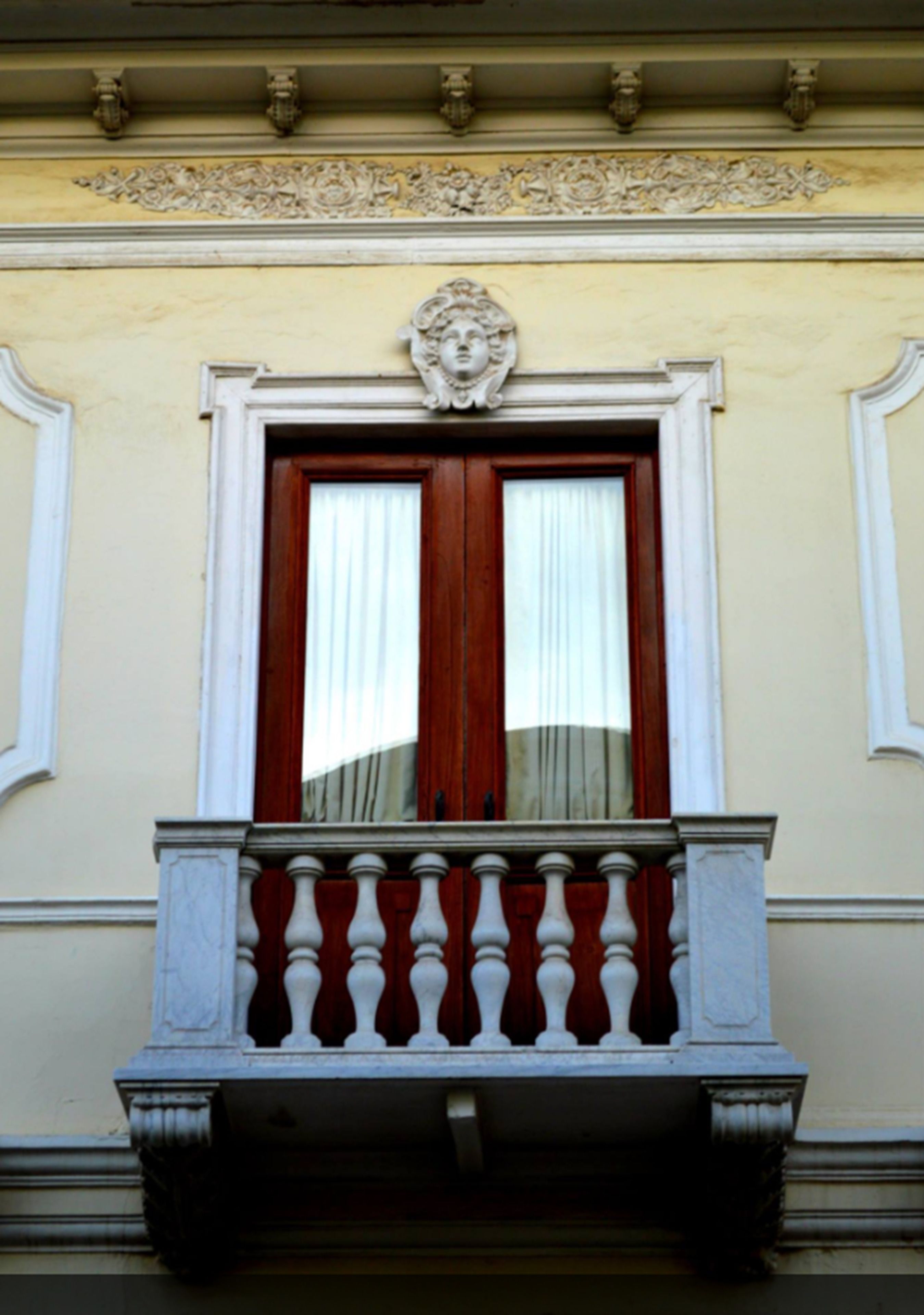 A building facade with a window featuring a balustrade and a decorative cornice.