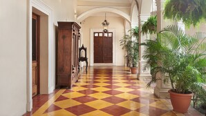 A hallway with a checkered floor, wooden doors, and a large potted plant. - Hotel La Perla (León)