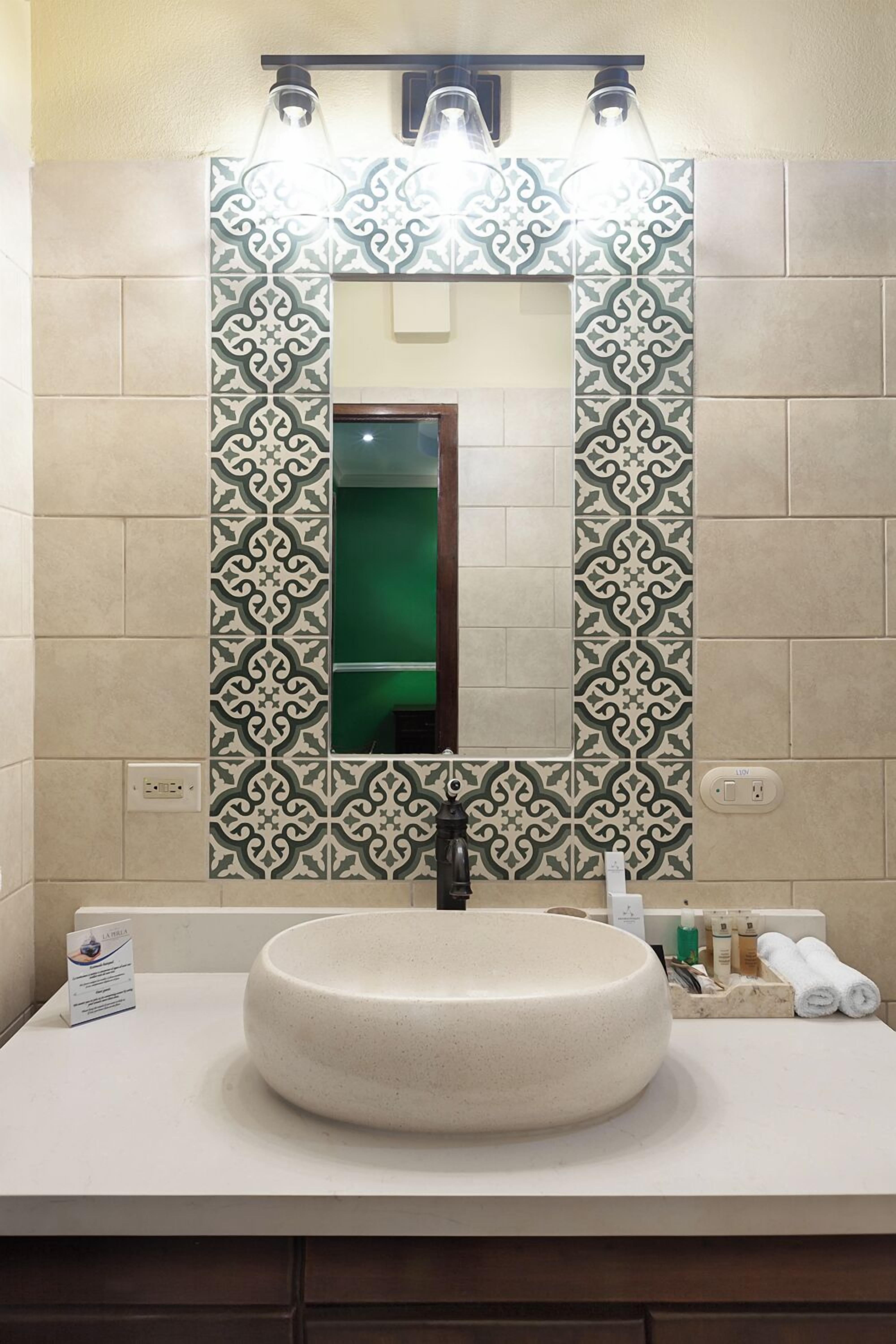 Un baño con un lavamanos redondo, un espejo y azulejos estampados.