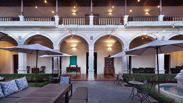An outdoor patio with wooden furniture, umbrellas, and a pool. - Hotel La Perla (León)