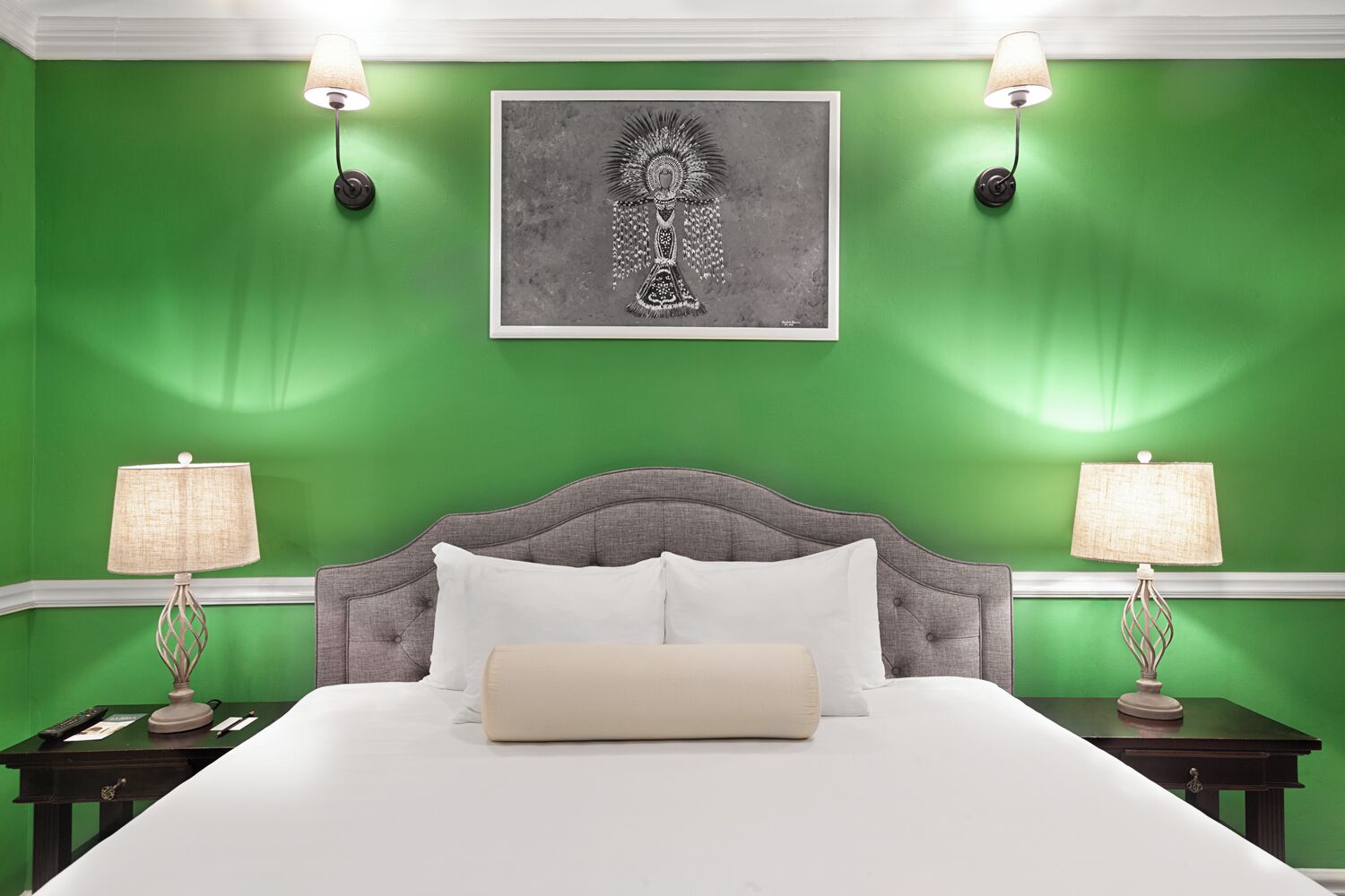 A bedroom with a green wall, a grey upholstered headboard, white bedding, and two bedside lamps.