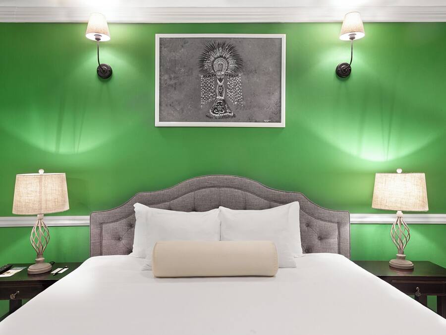 A bedroom with a green wall, a grey upholstered headboard, white bedding, and two bedside lamps.