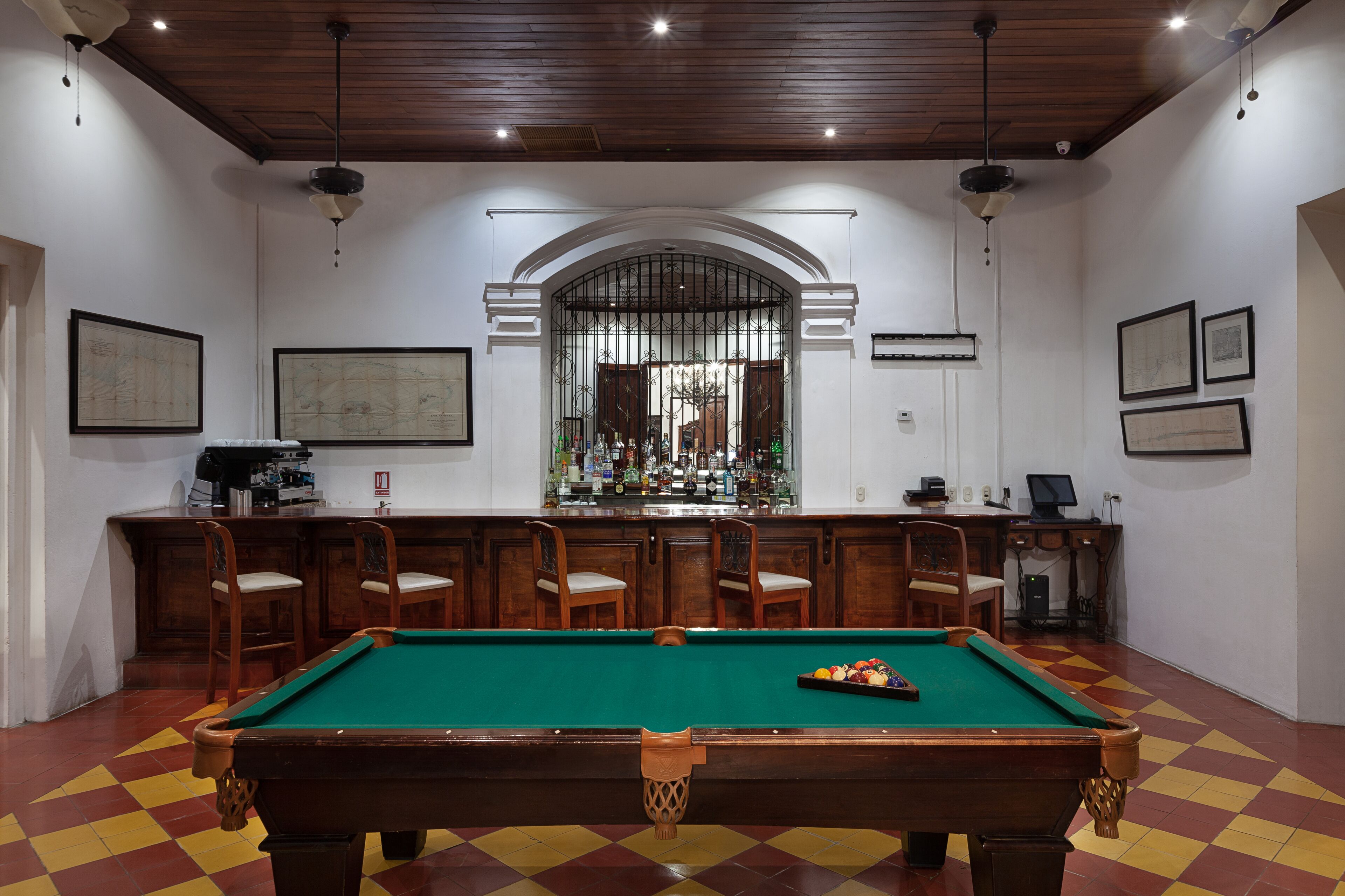 Una mesa de billar con sillas, una zona de bar y cuadros en las paredes.