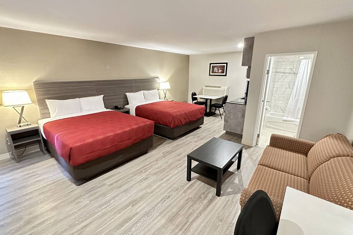 A hotel room with two beds, a desk, a chair, and a sofa.