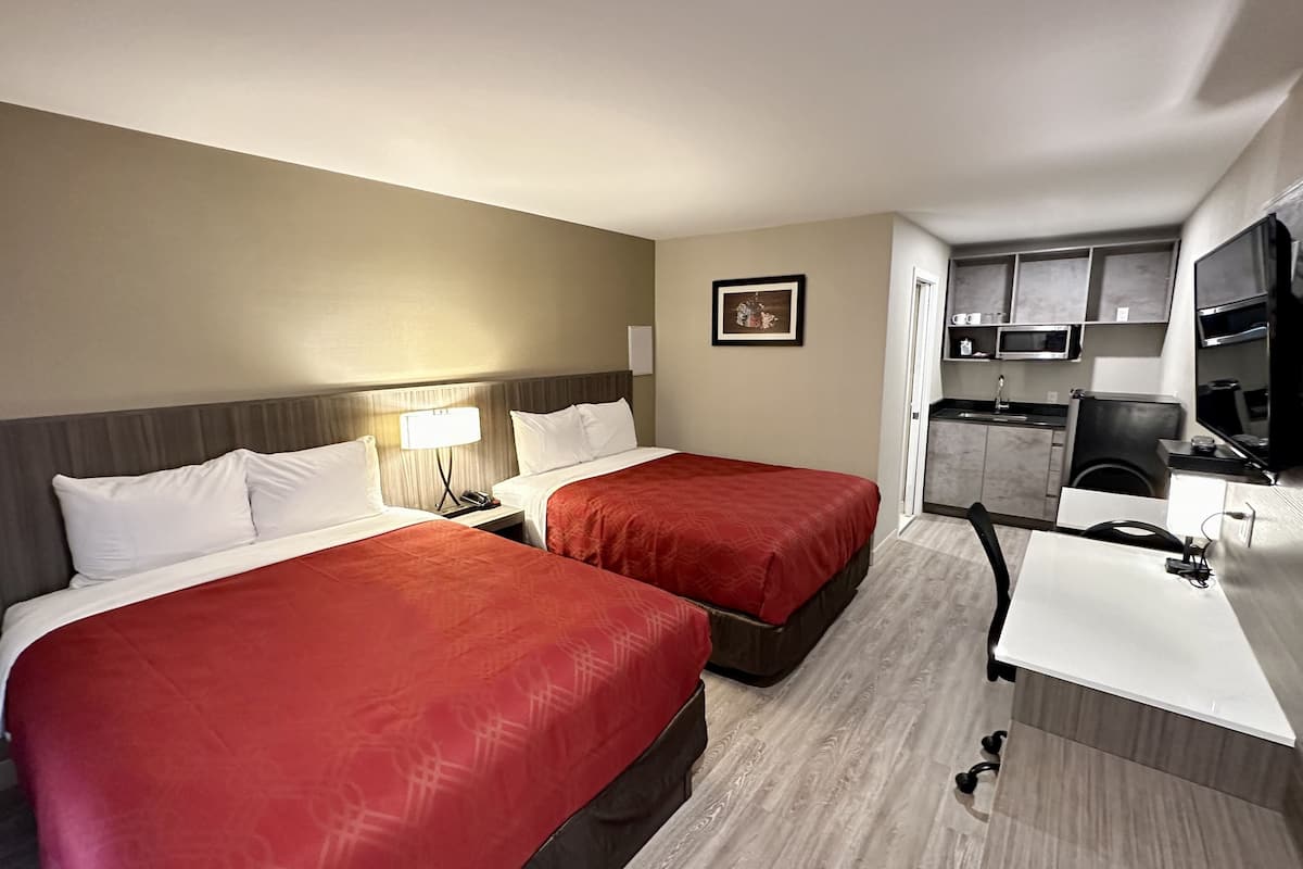A hotel room with two beds, a desk, a chair, a microwave, and a small kitchenette.