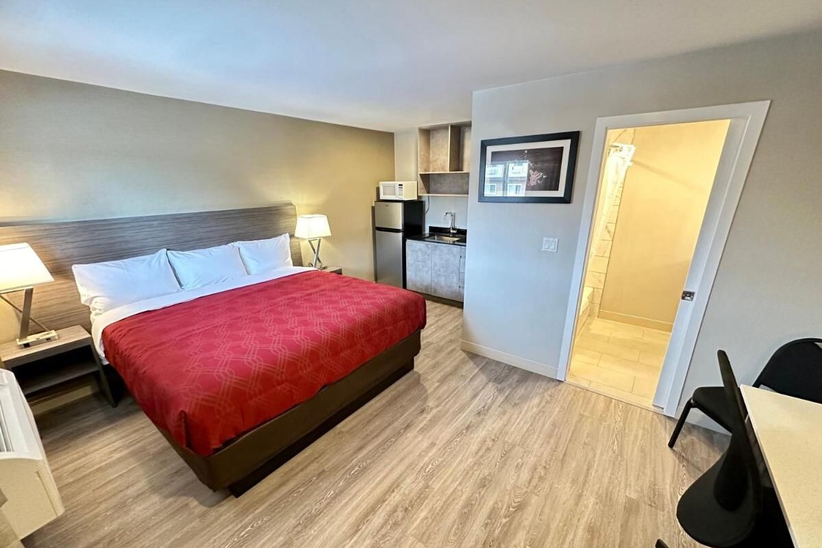 A hotel room with a bed, bedside tables, a desk, a chair, a microwave, and a small kitchenette.