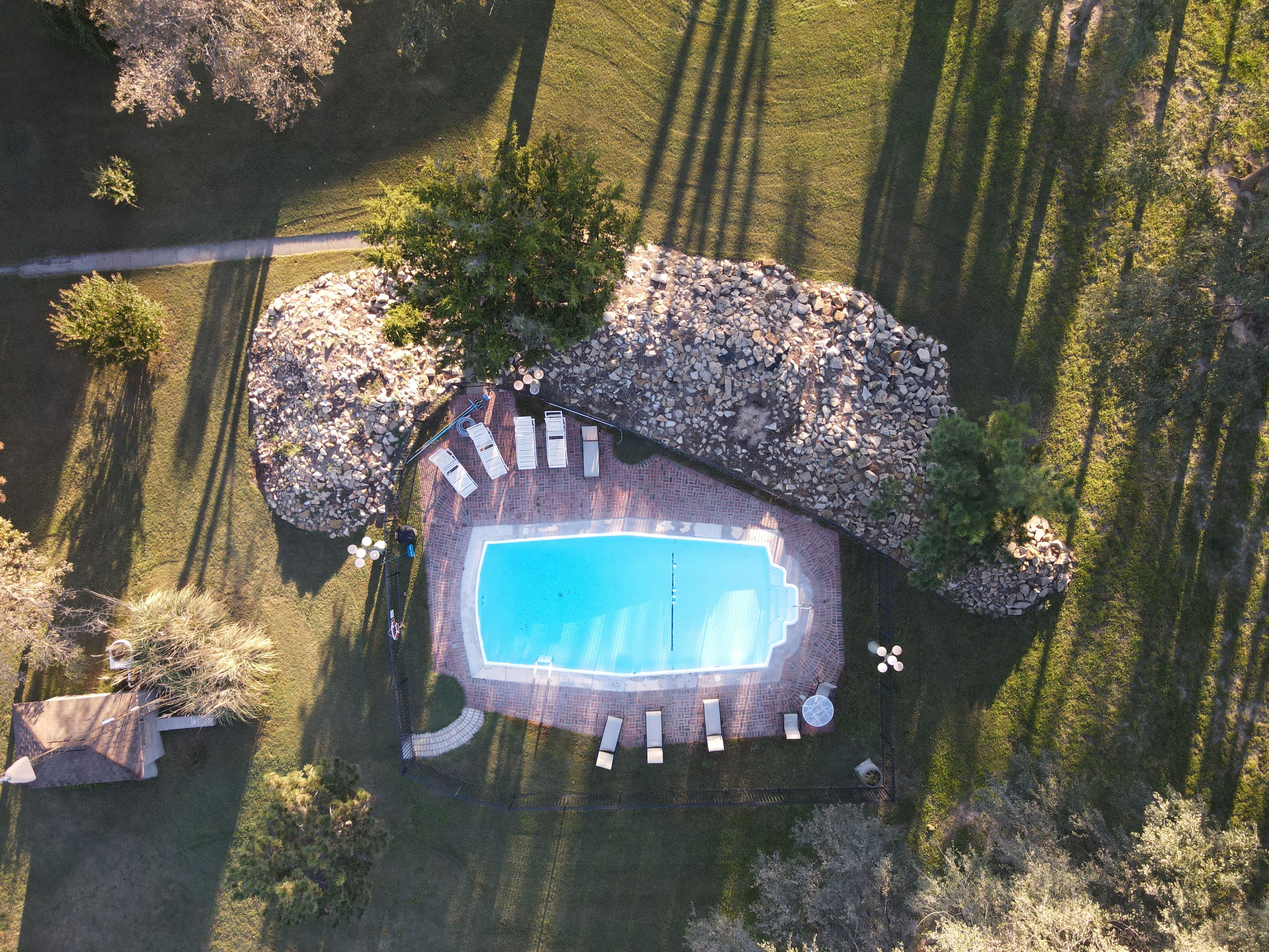 An aerial view of a property with a swimming pool, lounge chairs, and a stone patio.