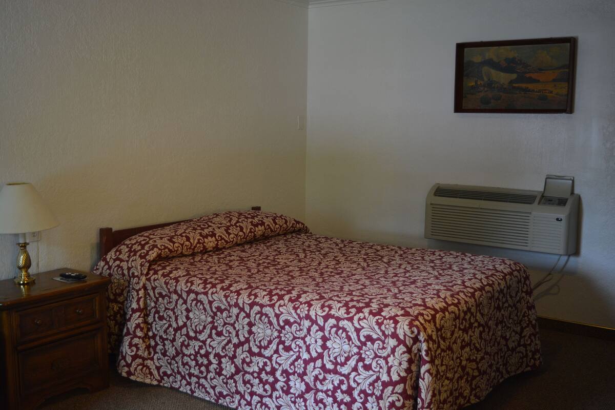 A single bed with a patterned bedspread, a bedside table with a lamp, and a wall-mounted air conditioner.