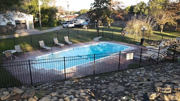 Una piscina rectangular con cerramiento metálico negro, rodeada por una terraza pavimentada y una zona ajardinada.