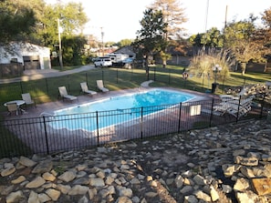 A rectangular swimming pool with a black metal fence, surrounded by a paved deck and a grassy area.