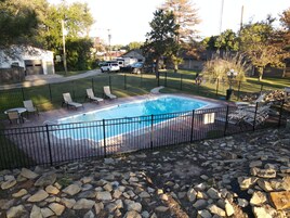 Una piscina rectangular con cerramiento metálico negro, rodeada por una terraza pavimentada y una zona ajardinada.