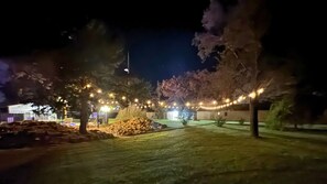 A nighttime outdoor area with string lights, trees, and a building in the background. - Evergreen Inn Kansas (Pratt)