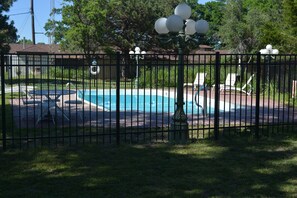 A fenced backyard with a swimming pool, lounge chairs, and a lamp post.