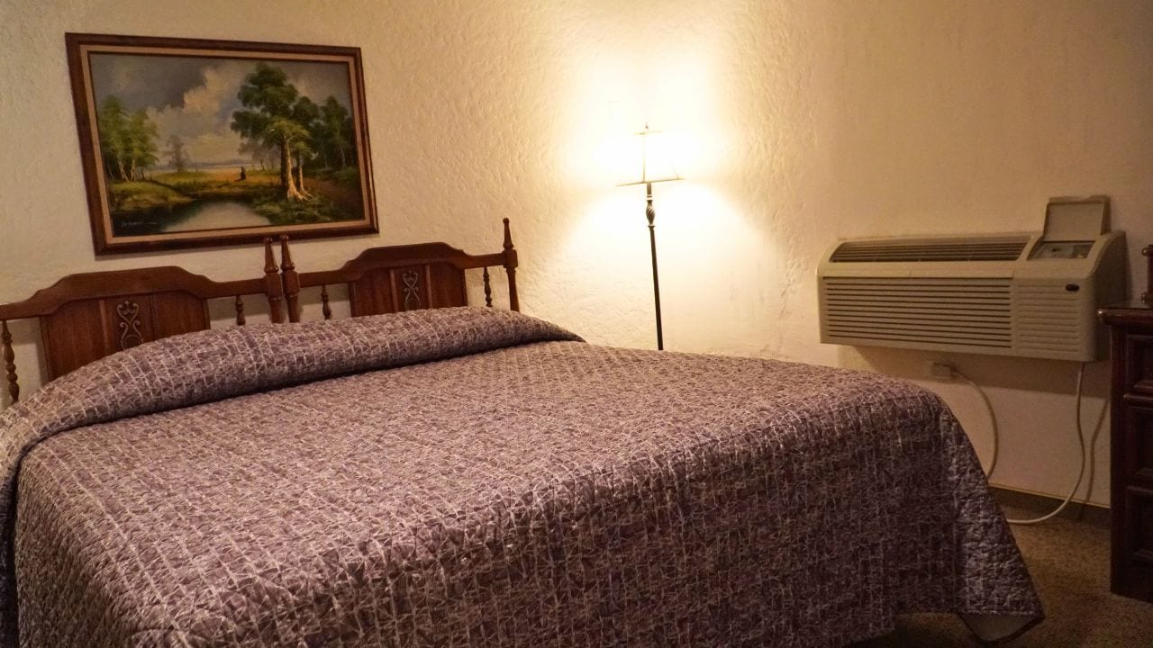 Un lit avec une couvre-lit à motifs, un tableau accroché au mur et un appareil de climatisation.