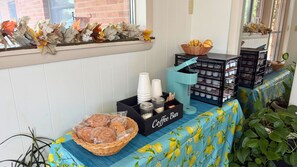 A coffee bar setup with baskets of bread, a coffee station, and decorative autumn leaves. - Evergreen Inn Kansas (Pratt)