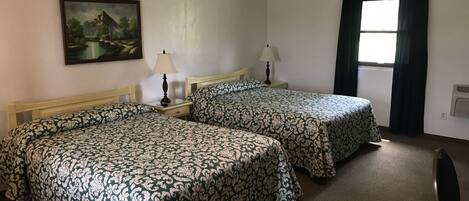 A hotel room with two beds, a painting on the wall, a window with curtains, and a radiator.