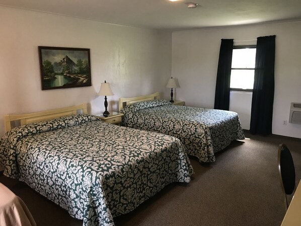A hotel room with two beds, a painting on the wall, a window with curtains, and a radiator.