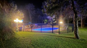 A fenced swimming pool area at night with artificial lighting. - Evergreen Inn Kansas (Pratt)