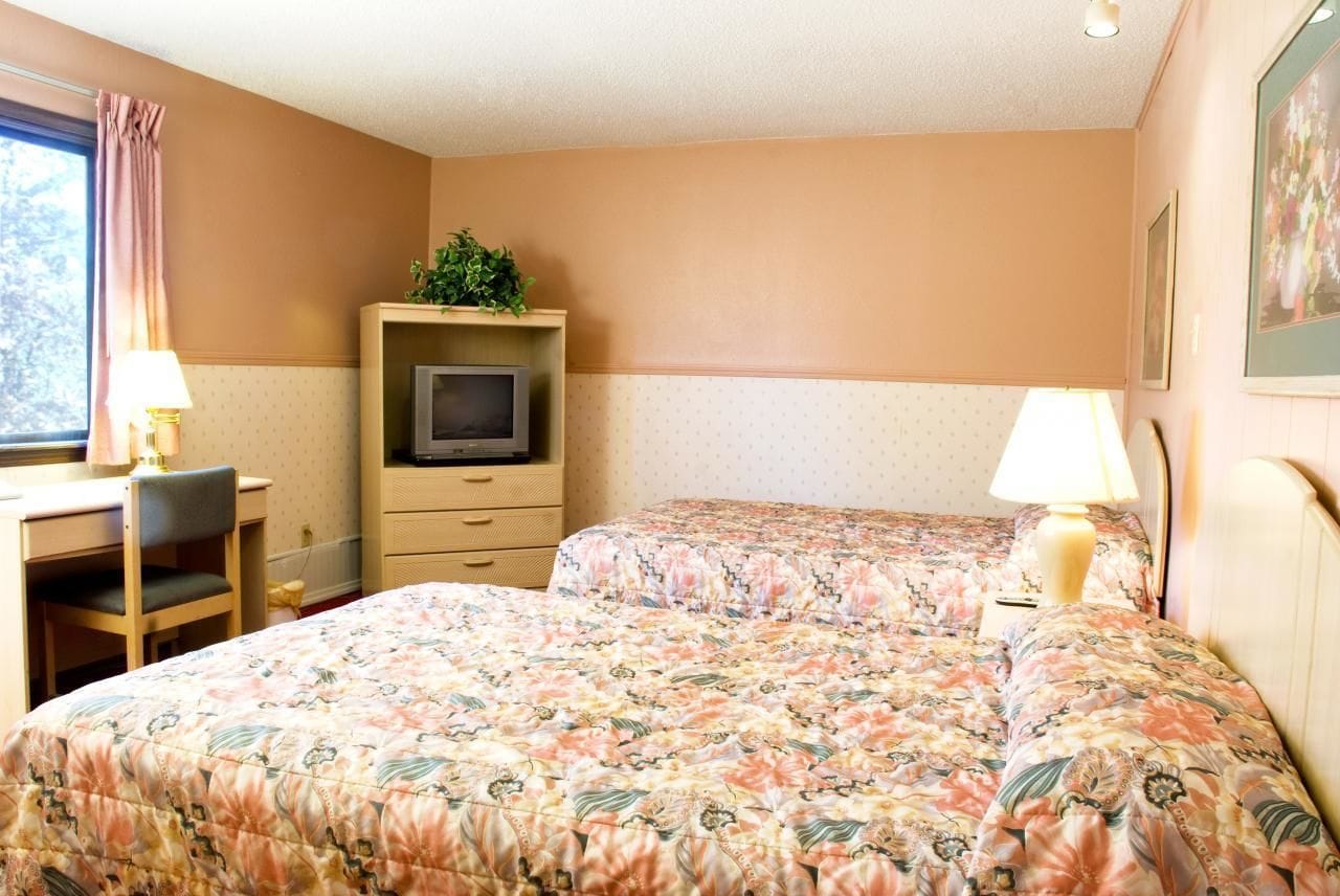 Habitación de hotel con dos camas, un escritorio, una silla, un televisor y una ventana con cortinas.