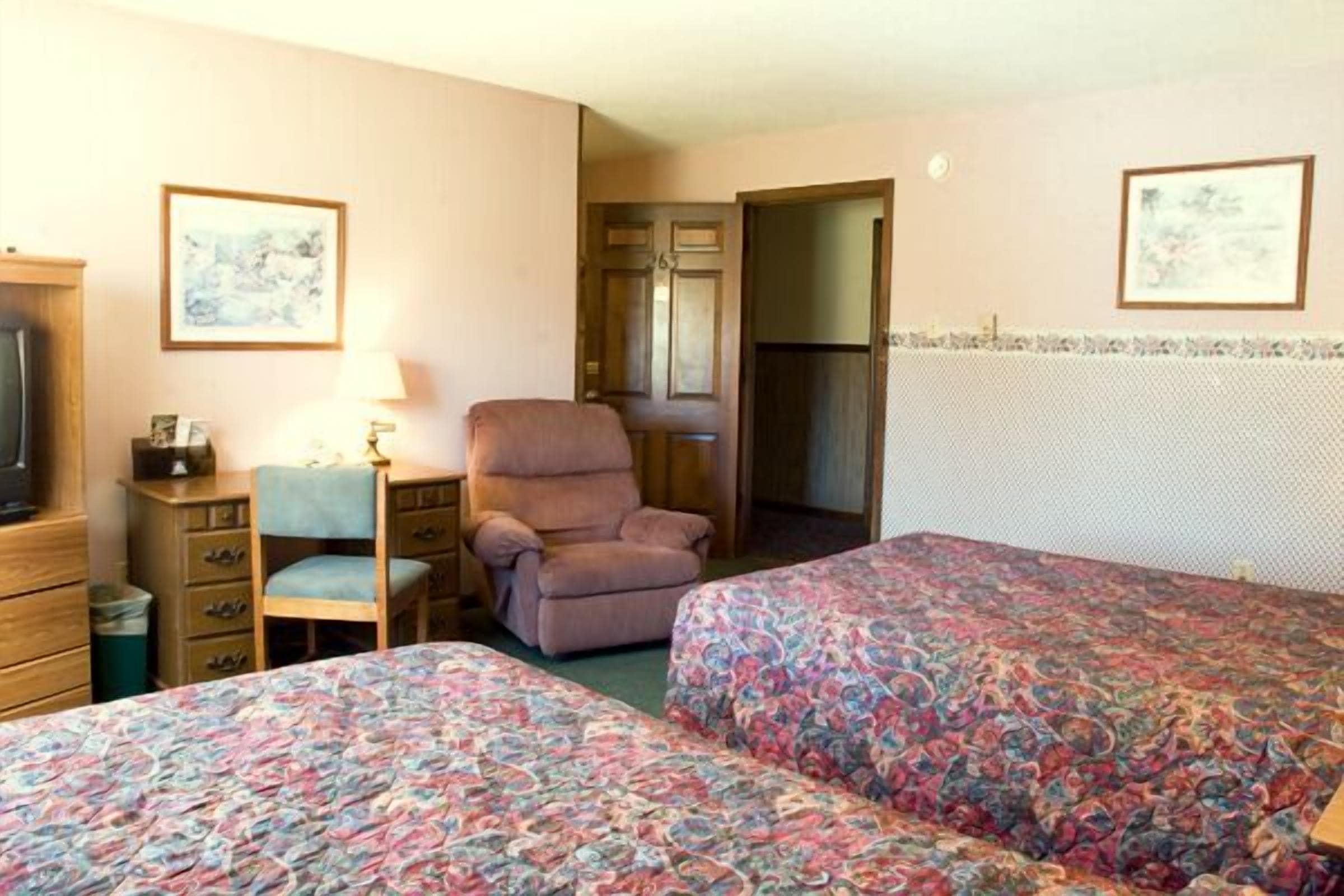 A hotel room with two beds, a desk, a chair, a dresser, and a television.