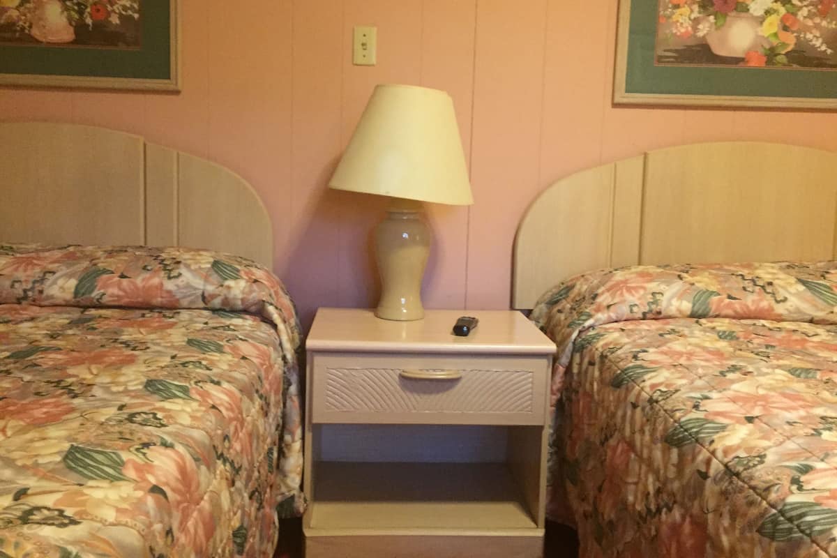 Habitación de hotel con dos camas, cada una con ropa de cama floral, una mesita de noche con lámpara y un cajón pequeño.