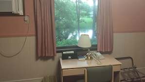Una habitación con escritorio, lámpara, teléfono y ventana con cortinas.
