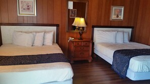 Une chambre d’hôtel avec deux lits, une commode en bois, un miroir et des œuvres d’art encadrées accrochées aux murs.