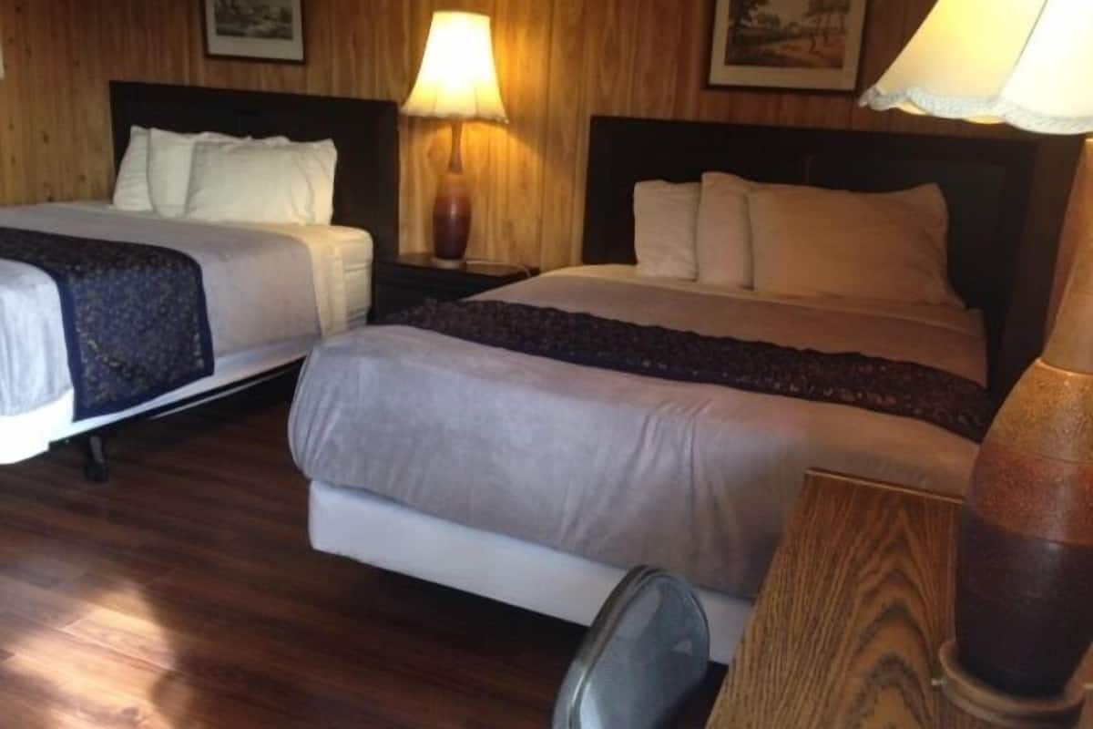 Une chambre d’hôtel avec deux lits, un plancher en bois et une lampe placée entre les deux.