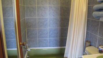 Un baño con una bañera verde, cortina de ducha y un inodoro.