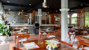 A modern restaurant with wooden tables and chairs, a glass dining area, and a kitchen in the background. - Tifakara by the Waterfall (La Fortuna)