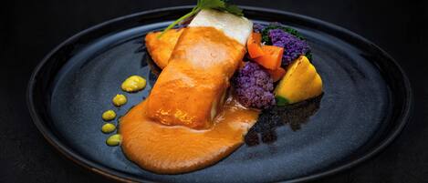 A dark plate with a salmon fillet, vegetables, and a garnish.