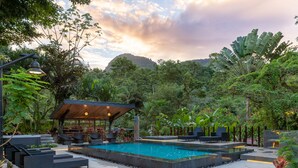 A pool area with seating and a covered structure, surrounded by lush greenery and a mountainous backdrop. - Tifakara by the Waterfall (La Fortuna)