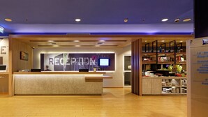 Zona de recepción de hotel con mostrador de recepción, señalización indicando las habitaciones de huéspedes y un directorio de servicios del hotel.