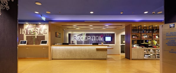 Zona de recepción de hotel con mostrador de recepción, señalización indicando las habitaciones de huéspedes y un directorio de servicios del hotel.