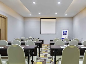 A conference room with tables, chairs, a projector screen, and a banner. - Hotel ibis budget Jakarta Airport (Tangerang)