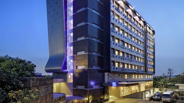 Un moderno edificio de hotel con un llamativo letrero 'ibis budget', varios pisos y una entrada bien iluminada.